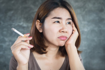 depressed Asian woman smoking cigarette with unhappy face sitting alone next to the wall  