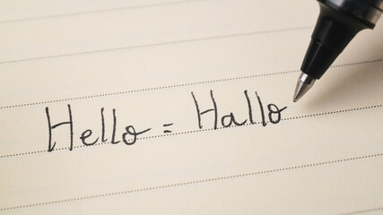 Beginner German or Dutch language learner writing Hello word Hallo for homework on a notebook