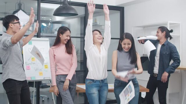 Group of Asia young creative people in smart casual wear celebrate project success and throwing documents in office. Diverse Asian male and female stand together at startup. Coworker teamwork concept.