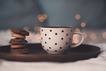 Cup of fresh hot tea with stack of chocolate cookies on wooden tray in bed close up. Good morning. Breakfast time. Focus on pastry.