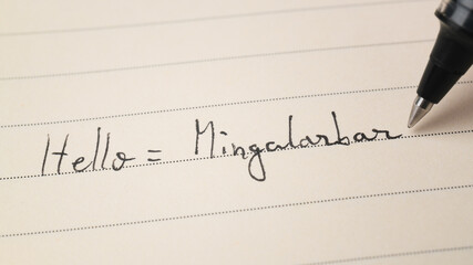 Beginner Burmese language learner writing Hello word Mingalarbar for homework on a notebook © Keitma