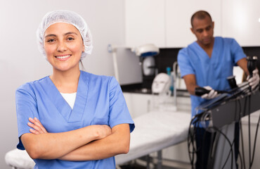 Smiling female cosmetologist standing in clinic of aesthetic medicine with arms crossed