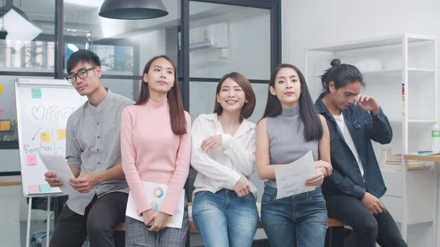 Group of Asia young creative people in smart casual wear looking at camera and smiling in creative office workplace. Diverse Asian male and female stand together at startup. Coworker teamwork concept.