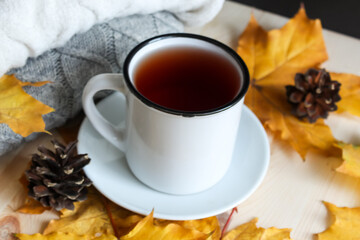 Autumn background. Autumnal leaves, pine cones, cup of tea and sweater on wooden background.