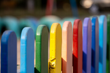 Part of wooden, rainbow colorful painted fence  on a sunny hot summer day in a city park. Abstract multicolored background.