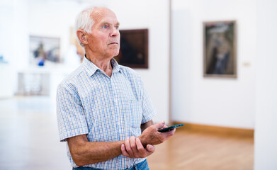 mature European man examines paintings in an exhibition in hall of an art museum