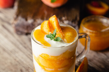 Peach fruit dessert in glass cup on wooden table. Homemade dessert with fruits. Fruit salad with yogurt or sour cream. Close up