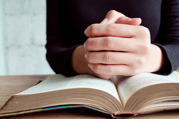 Pray in the Morning, Woman praying with hands together, Woman praying while holding Bible And some of the blurred text in Bible
