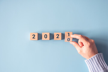 Hand flipping wooden blocks for change year 2020 to 2021 on blue paper background. New year and...