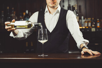 Male sommelier pouring white wine into wineglasses.