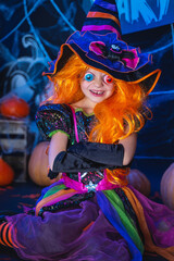 Fototapeta premium Little beautiful girl in a witch costume celebrates Happy Halloween party in interior with pumpkins.