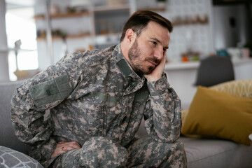 Depressed soldier sitting on sofa in living room. Young marine having PTSD..