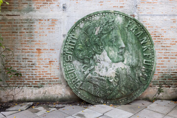 front view of old broken stone sculpture coin on brick cement wall