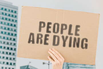 The phrase " People are dying " on a banner in men's hand with blurred background. Deaths. Hazardous. Statistics. Analysis. Mortality rate. Dangerous. Population. Bad