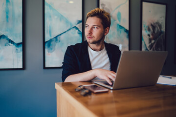Fototapeta premium Young man using laptop and looking away in office