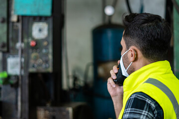 Technical supervisor wearing a mask is operating a crew through a radio communication in the...