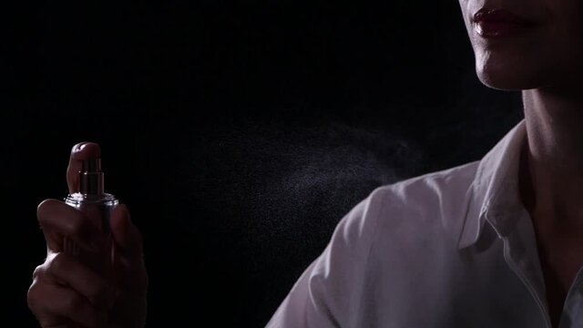 Woman spraying on perfume against black background, closeup. Slow motion