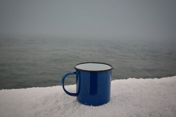 Blue enamel mug in the snow by the sea.  Bosphorus. Istanbul.