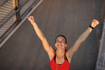 Above view of happy athletic woman with raised arms celebrating outdoors.