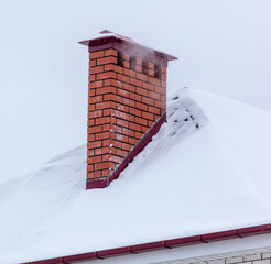 Brick chimney in the snow on the roof of the house.