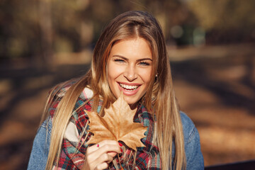 Portrait of a beautiful blonde with a smile on face holding a leaf in hand in the park