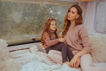 Happy family - mother and little daughter relaxing hugging and having fun in countryside inside white scandinavian rustic camper van interior. Domestic tourism concept.