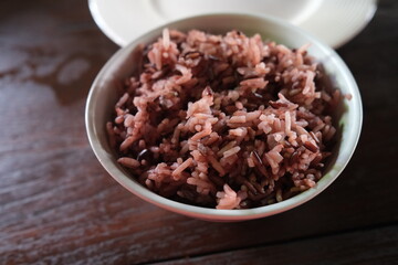 selective focus on reddish-black whole-grain rice in white bowl on the wooden table