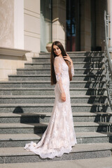 Fototapeta premium Gorgeous model in wedding dress stand on stair by big restaurant