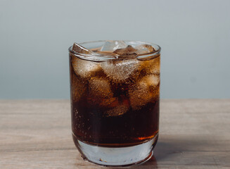 Close up cola and ice cube in clear glass on wooden table