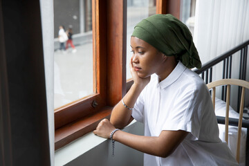 Portrait of sad African young woman cancer patient fighting with the sickness, wearing head scarf after suffering serious hair loss side effect due to chemotherapy, concept of cancer awareness