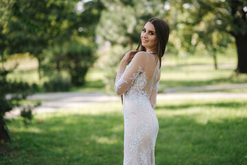 Gorgeous young woman in wedding dress stan outdoors in front of green trees