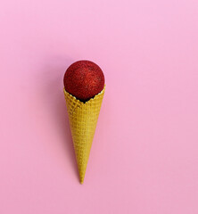 Waffle cone with a Christmas tree ball on a pink background.