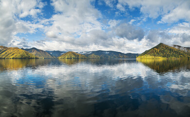 Beautiful reflection in the water of the mountains and sky. The calm flow of the Yenisei River in Siberia. Autumn view.