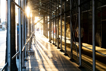 Sunlight shining through construction scaffolding above an empty sidewalk in Manhattan, New York...