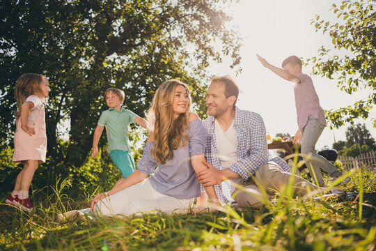 Full length photo of loving family have summer outside weekend garden rest mom mommy dad daddy sit blanket little kids play under tree sunshine sunset