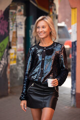 beautiful girl in black clothes stands with a cup of coffee in the city