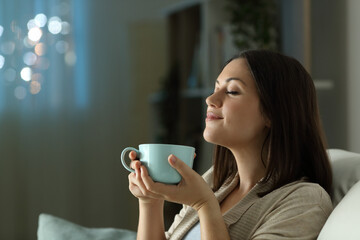 Woman relaxing smelling coffee in the night at home