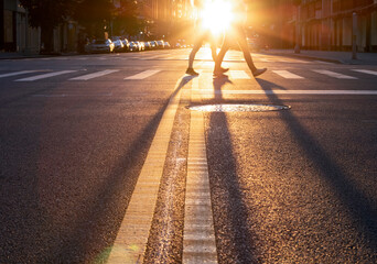 Man and woman walking across the street in New York City with the light of sunset casting long...