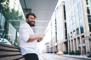 Cheerful businessman browsing tablet on public transport stop