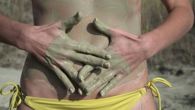 Woman smears skin with cosmetic mud or clay outdoors