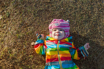 Cheerful toddler child lies on the ground in winter colorful clothes without snow