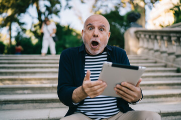 Fototapeta premium Amazed senior man using tablet on stairs in park