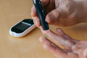 diabetes, healthcare - close up of a man with a glucometer and a test strip checking blood sugar at home