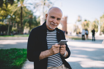 Happy aged man using smartphone in modern park
