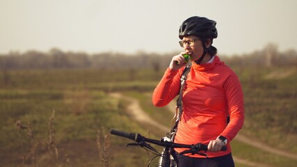 Athletic Caucasian woman eats protein bar ride on mountain bike on nature. Young sporty woman...