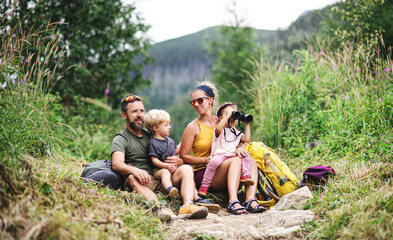 Family with small children hiking outdoors in summer nature, sitting and resting.
