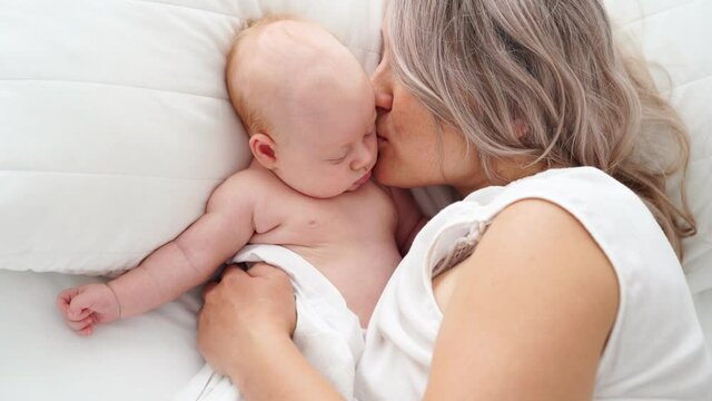 mother kisses sleeping baby lying in bed. concept of maternal love, newborn care