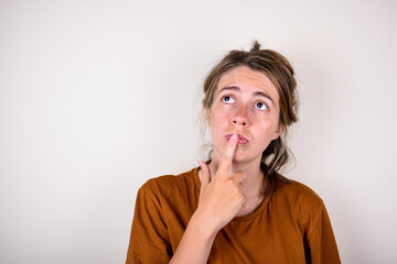 young pensive woman in a brown t-shirt put her finger to her face isolated on a light background. Concept for ideas or reflections.