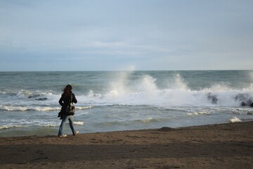 the rough sea during the bad weather. High waves come ashore in a windy autumn afternoon. A girl walks on the shore to see the natural spectacle. Ostia, Rome