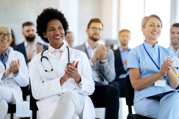 Happy African American doctor applauding while attending healthcare seminar.